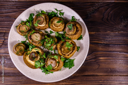 Plate with baked champignons, dill and parsley on a wooden table. Top view