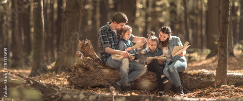 Family together reading books in the forest .