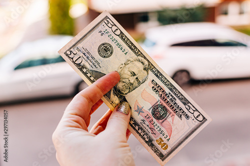 Female hand holds 100 dollar bill against the background of the street. US 50 dollar bill close up, USA federal fed reserve note. photo