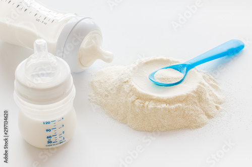 Baby food. Powder in spoon near baby bottle on white background