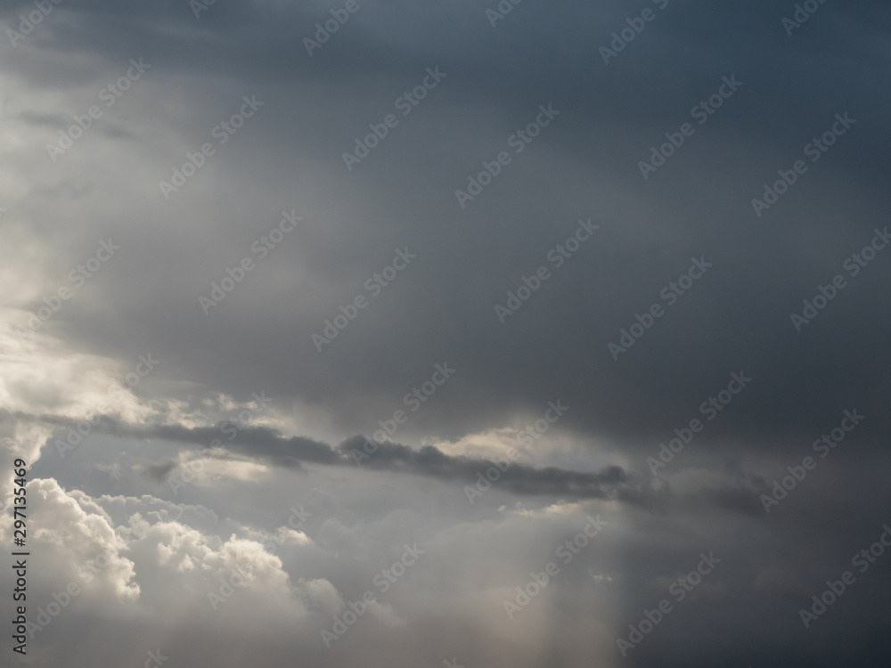 Cloudy dramatic sky over a forest silhouette, sun rays.