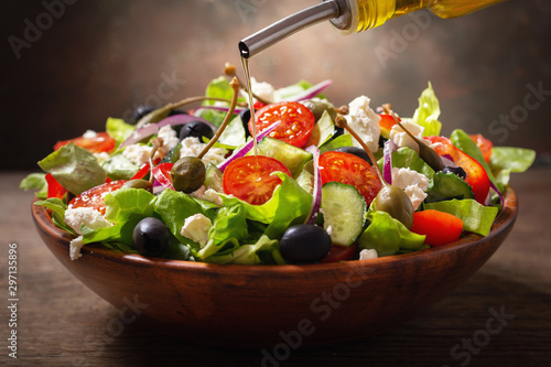 Photo olive oil pouring into bowl of fresh salad with vegetables, feta cheese and cape