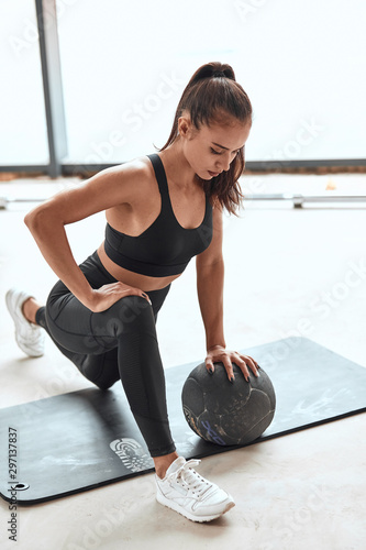 Attractive athletic girl stretch legs in gym. Using medballs in fitness. Window background photo