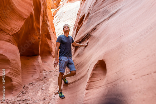 Man hiker looking up touching wall of red wave shape formations at Antelope slot canyon in Arizona on footpath trail from Lake Powell