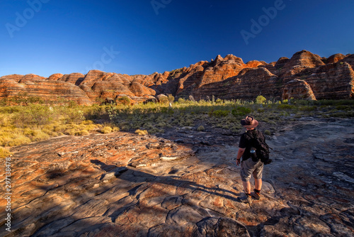 Nature photographer on a hiking trip at the Australian outback between dome of rocks with blue sky at the morning light