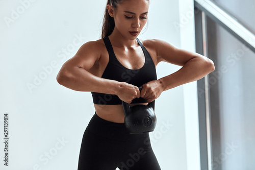 фотографія Young athletic and strong female holding, lifting up kettlebells with two hands