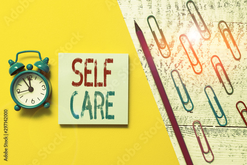 Handwriting text Self Care. Conceptual photo the practice of taking action to improve one s is own health Notepad marker pen colored paper sheet clips alarm clock wooden background