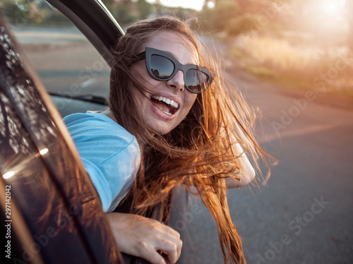 Young pretty brown-haired girl enjoys feeling the wind while leaning out of the car window