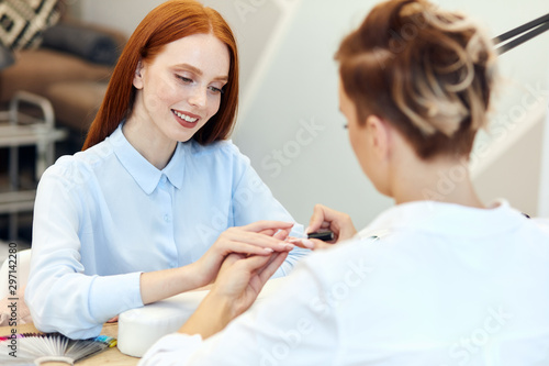 Wallpaper Mural Redhead caucasian girl smiling in manicure salon. Manicurist and client dressed in white shirts. Enjoy beauty procedure Torontodigital.ca