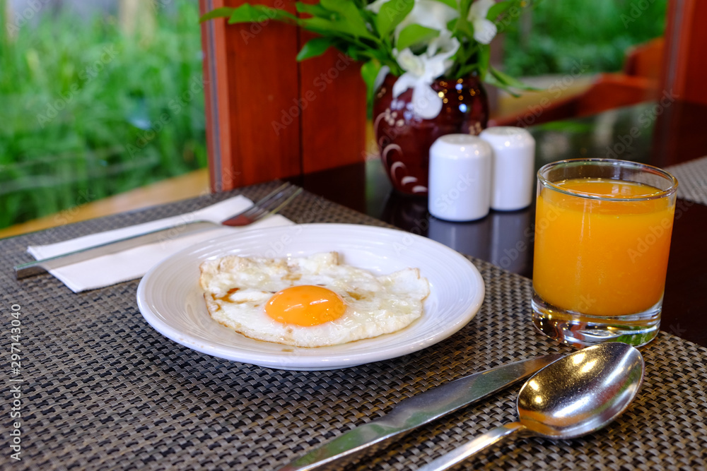 Sunny side up fried egg served on white dish with orange juice for breakfast Sunny side up fried egg served on white dish with orange juice for breakfast