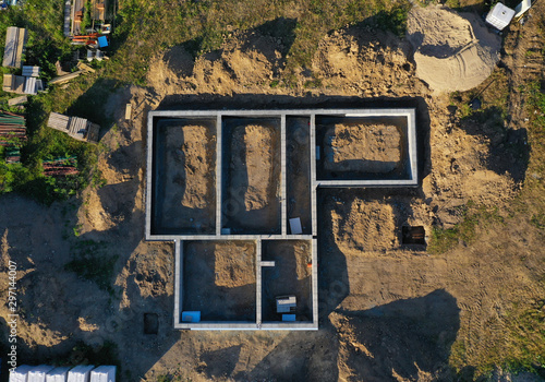 Aerial drone top down view on construction site with reinforced concrete house foundation, brick wall and materials like wall blocks and sand