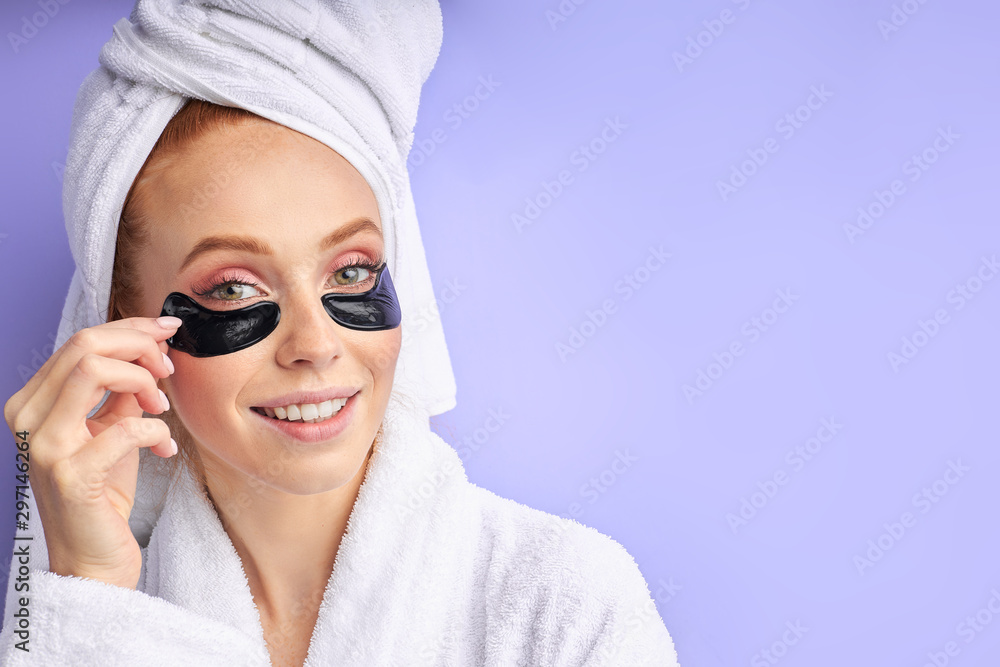 Attractive caucasian woman in bathrobe and towel posing with black patches look at camera , beauty industry, skin care. Isolated over purple background Attractive caucasian woman in bathrobe and towel posing with black patches look at camera , beauty industry, skin care. Isolated over purple background
