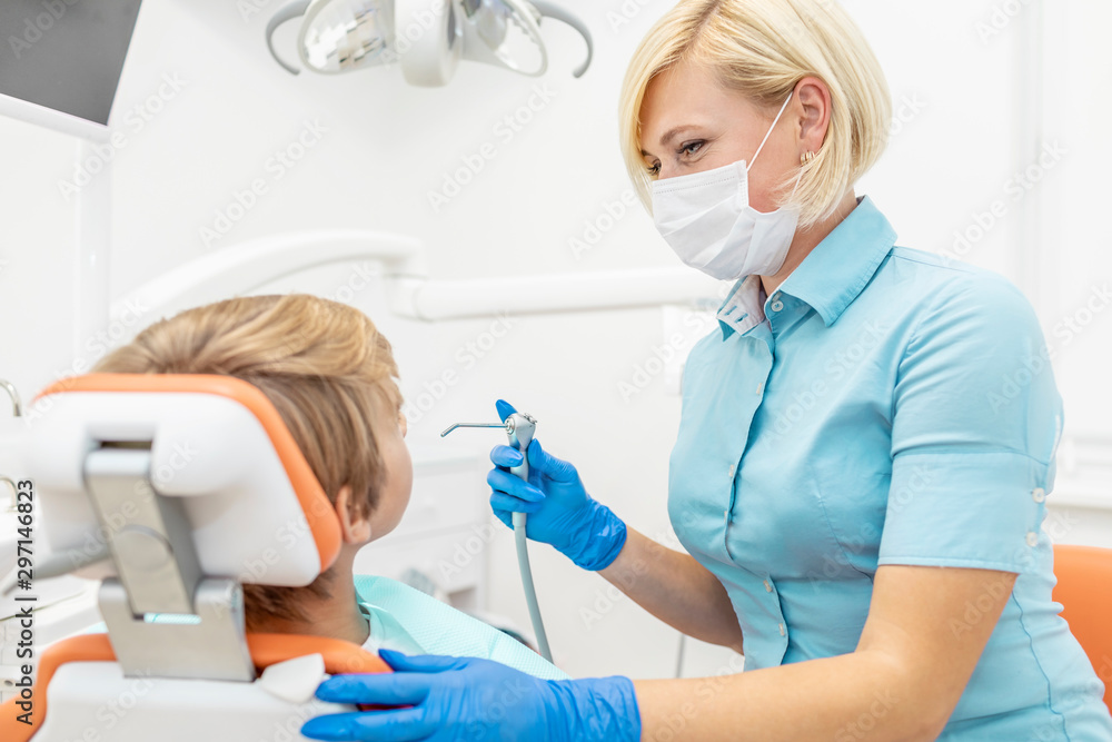 Female pediatric dentist with smiling eyes using water spray syringe to cleanse young patient's mouth Female pediatric dentist with smiling eyes using water spray syringe to cleanse young patient's mouth