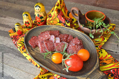 Salami sausage on wooden cutting board on dark background, matroshka dolls and khokhloma style in decoration photo