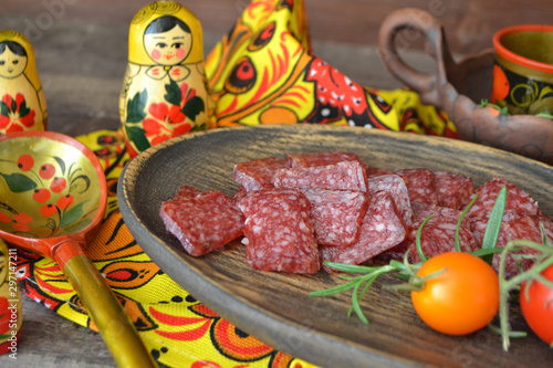 Russian salami sausages sliced on rustic wooden plate, bright matroshka dolls, spoon khokhloma photo