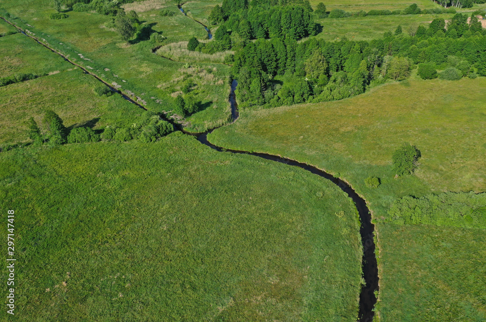 Aerial drone perspective view on european green meadows and forest divided by snake like river