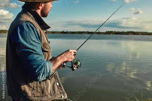 Print op canvas Caucasian adult bearded men stand near lake and hold fishing rod