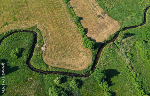 Aerial drone top down view on european green meadows, wheat fields and forest divided by snake like river.