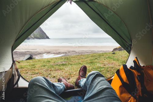POV view of hipster tourist inside tent on front of mountains and sea. Adventure travel lifestyle wanderlust