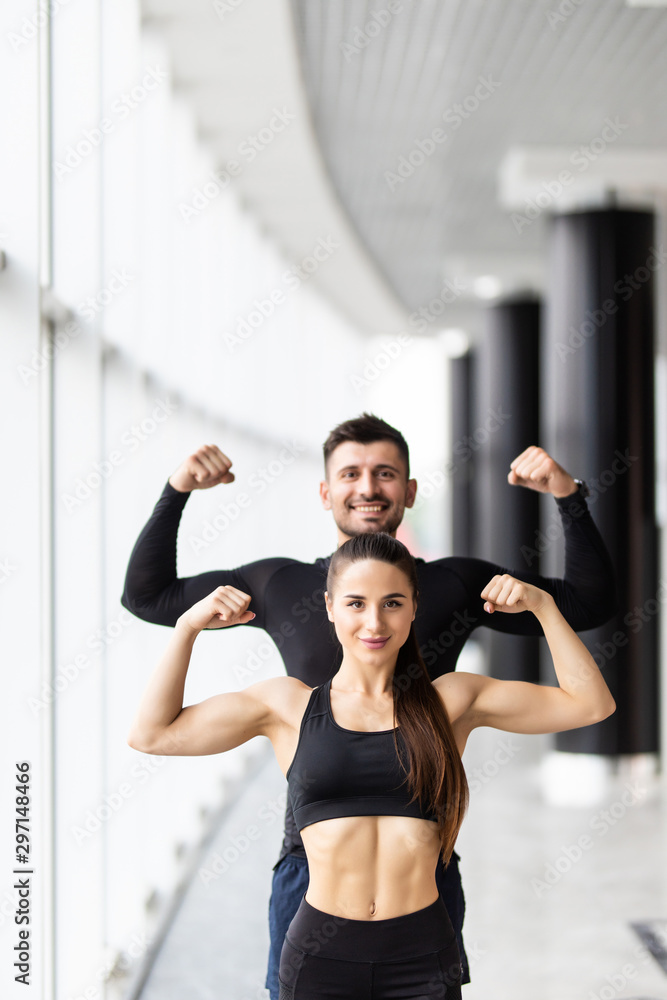 Obraz premium Athletic man and woman after fitness exercise show biceps standing at gym