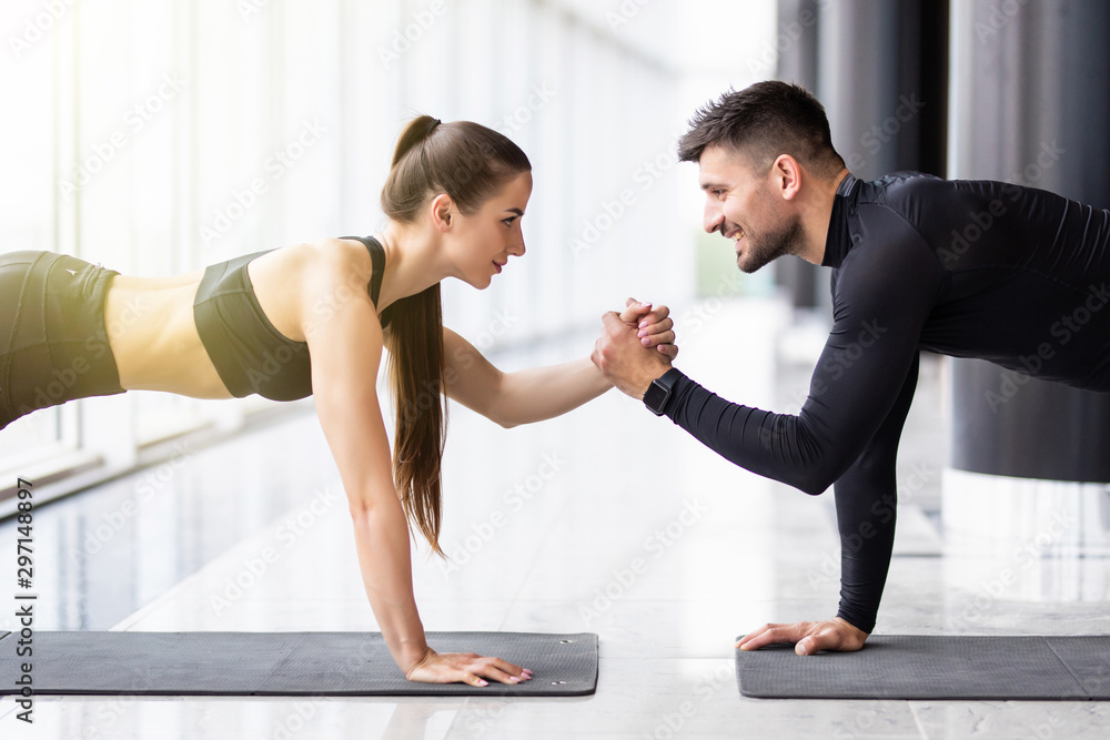 Slim girl and strong man are standing in one hand plank position and balancing on that hand. - obrazy, fototapety, plakaty 