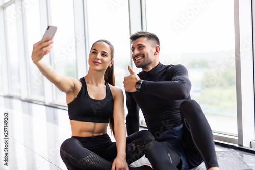 Young couple making selfie at gym. Athlete man and woman taking photo on smartphone having break after training 