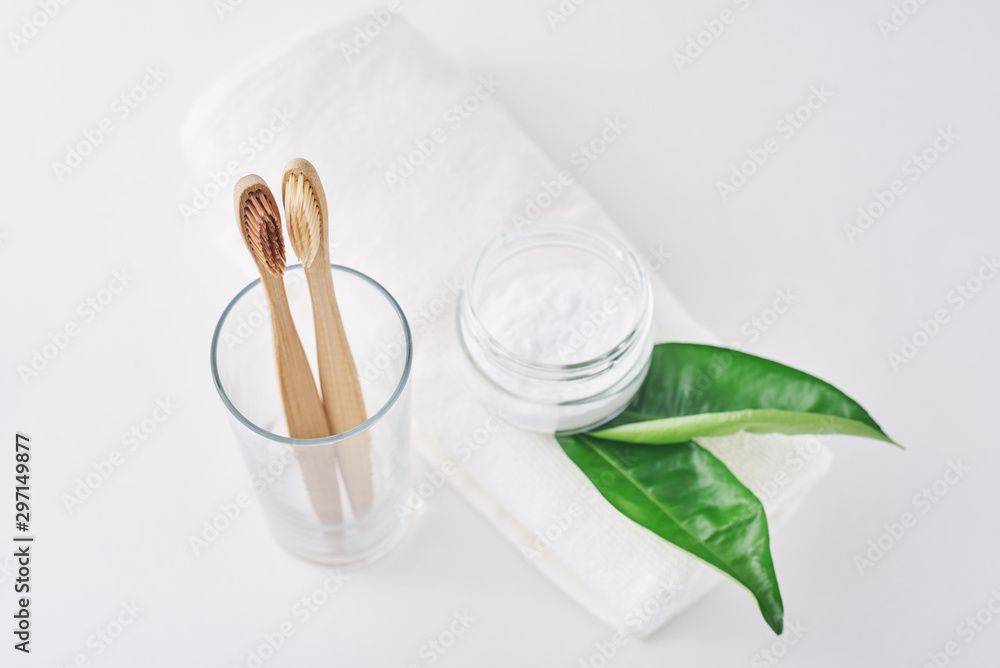 Two wooden bamboo eco friendly toothbrushes in a glass, baking soda and towel on white background.  Dental care and zero waste concept