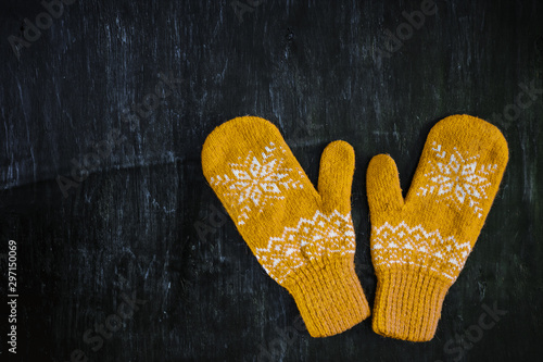 a pair of yellow orange knitted mittens on a dark blue-green-brown wooden