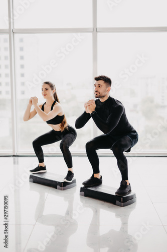 Fit couple working out make squats together at gym