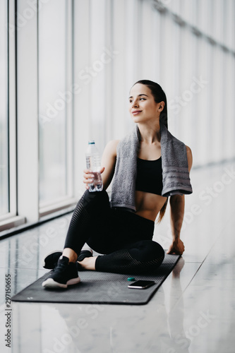 Sport woman sitting and resting after workout or exercise in fitness gym with protein shake or drinking water on floor. Relax concept.