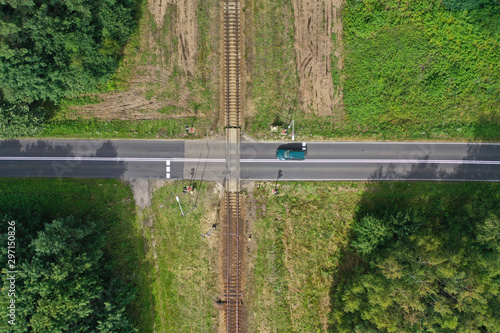 Aerial drone top down view on railroad crossing with asphalt road in the forest with car passing