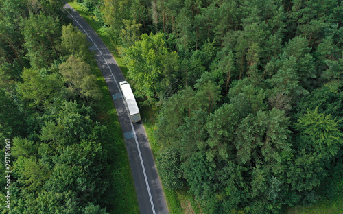 Fototapeta Naklejka Na Ścianę i Meble -  Aerial drone perspective view on white truck with cargo trailer riding through the forest on curved asphalt road