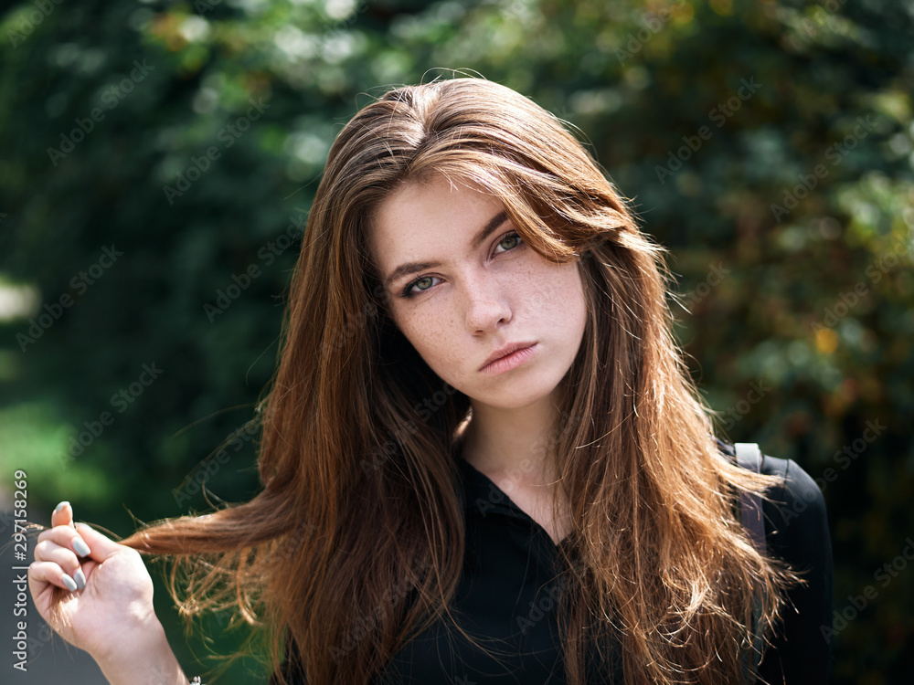 Closeup portrait of young natural beautiful redhead woman in black blouse playing with her natural long hair against blurred green foliage park background windy weather Closeup portrait of young natural beautiful redhead woman in black blouse playing with her natural long hair against blurred green foliage park background windy weather