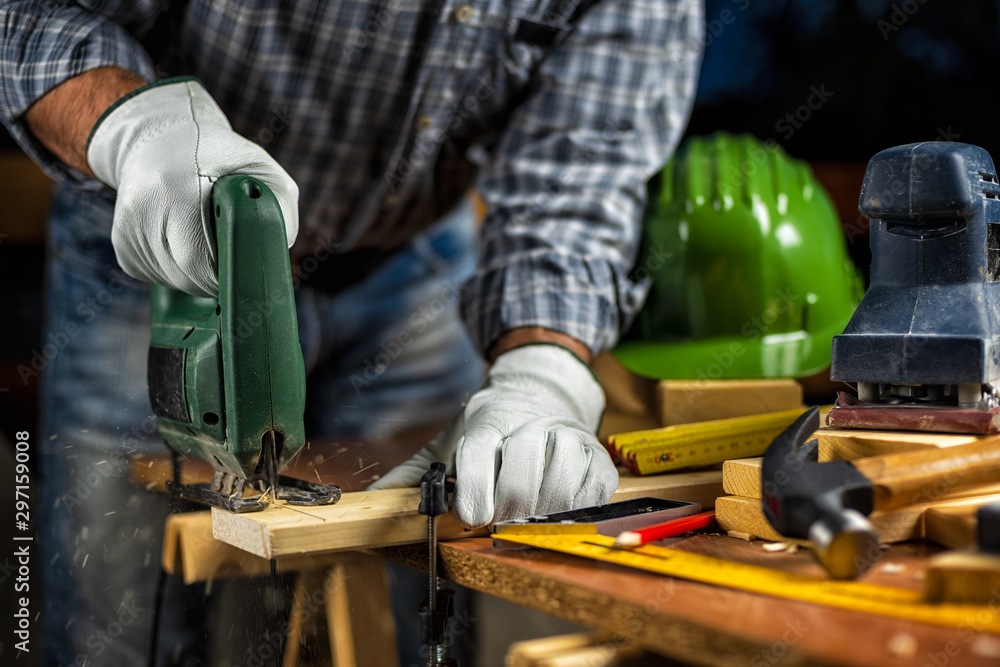 © francescomou - Adult carpenter craftsman wears protective leather gloves, with electric saw working on cutting a wooden table. Construction industry, housework do it yourself. Stock photography.