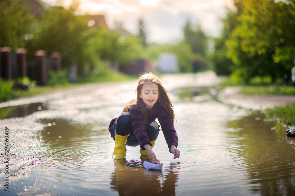 girl in yellow sopog plays in a puddle in a small boat, children's fun girl in yellow sopog plays in a puddle in a small boat, children's fun