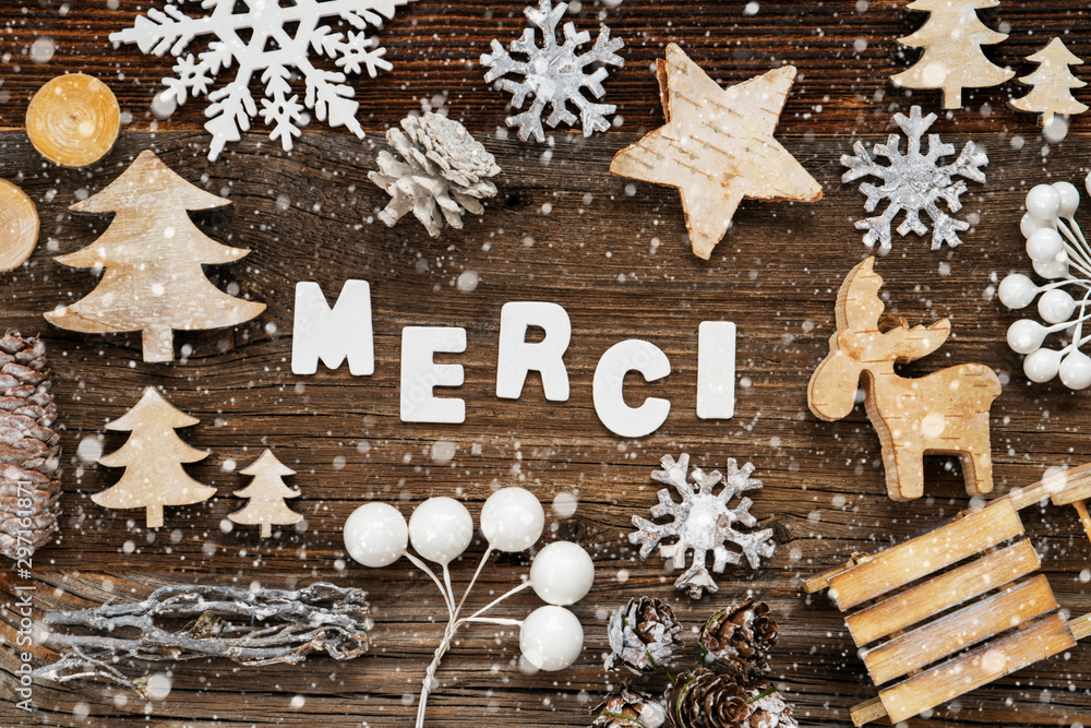 White Letters Building The Word Merci Means Thank You. Wooden Christmas Decoration Like Tree, Sled And Star. Brown Wooden Background With Snowflakes