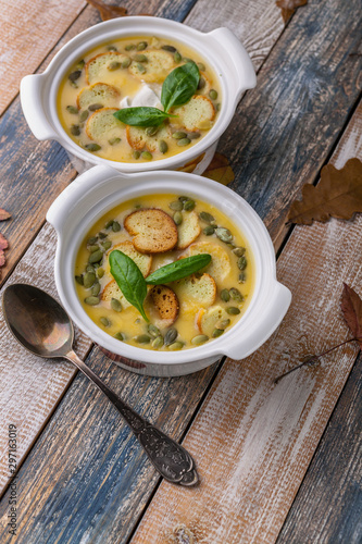 Two servings Autumn cream soup with vegetables, croutons, pumpkin seeds and fresh spinach on a rustic background. Vertical shot