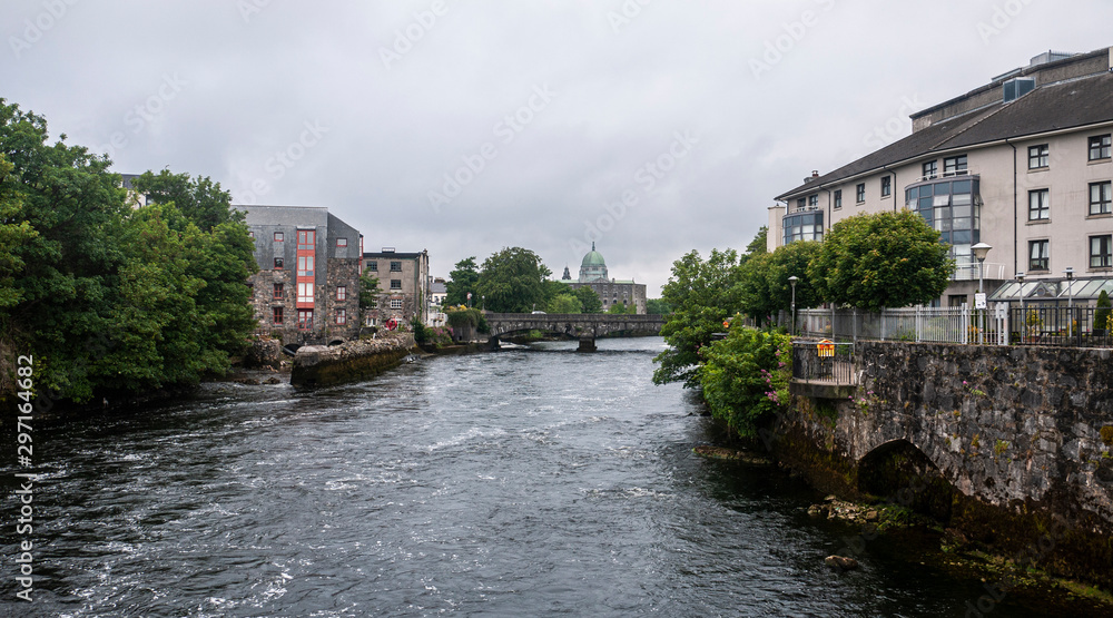 View of the River Corrib flowing through Galway City Center with the old stone buildings and walkways through the quays and view of the Cathedral