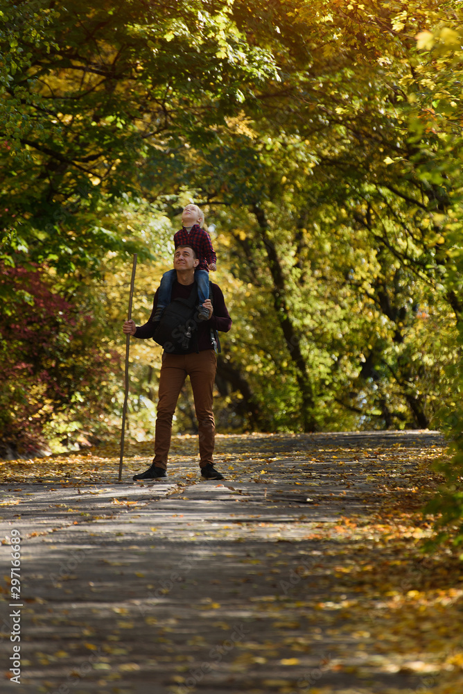 Fototapeta premium Father with son on his shoulders walking in the autumn park.