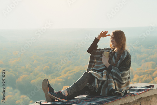 Young pregnant woman with sits on a hill and looks into the distance. Enjoying a sunny day