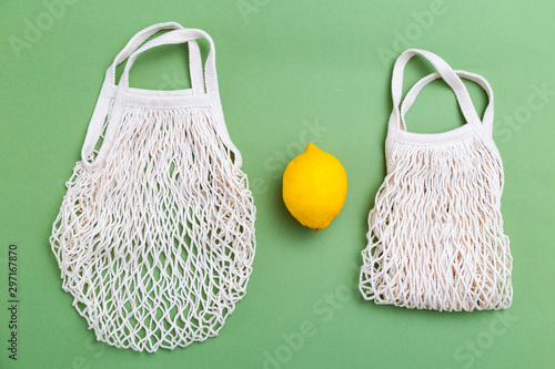 Reusable mesh bags with lemon on green background. Flat lay