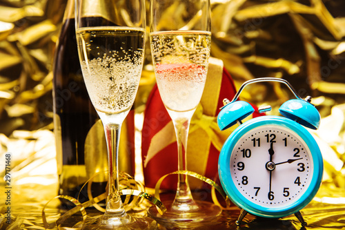 Time to celebrate. Close up photo of two glasses of champagne and a sky blue alarm clock, which shows quarter past twelve with bottle of champagne and a red box on the background.