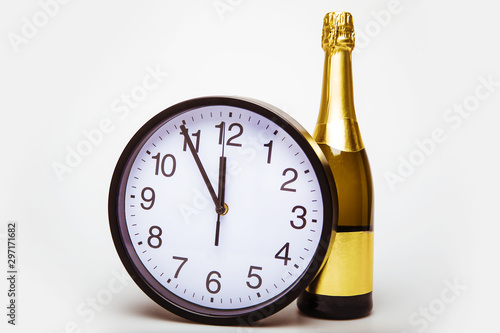 Expectation. Close up of a big black and white clock, which shows five minutes to twelve, placed near unopened bottle of champagne.