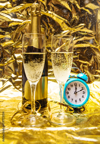 Golden day. A composition of two glasses of champagne, an unopened bottle of champagne and a sky blue alarm clock which shows ten past twelve.