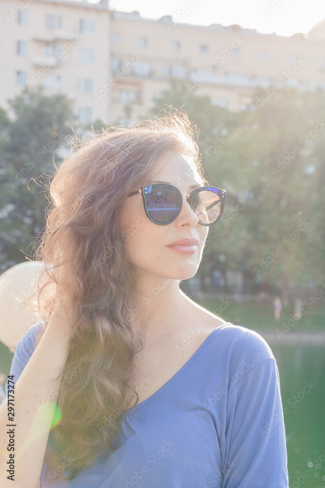 Portrait of a young handsome girl in sunglasses with dark hair against the sun. Close - up solar portrait Portrait of a young handsome girl in sunglasses with dark hair against the sun. Close - up solar portrait