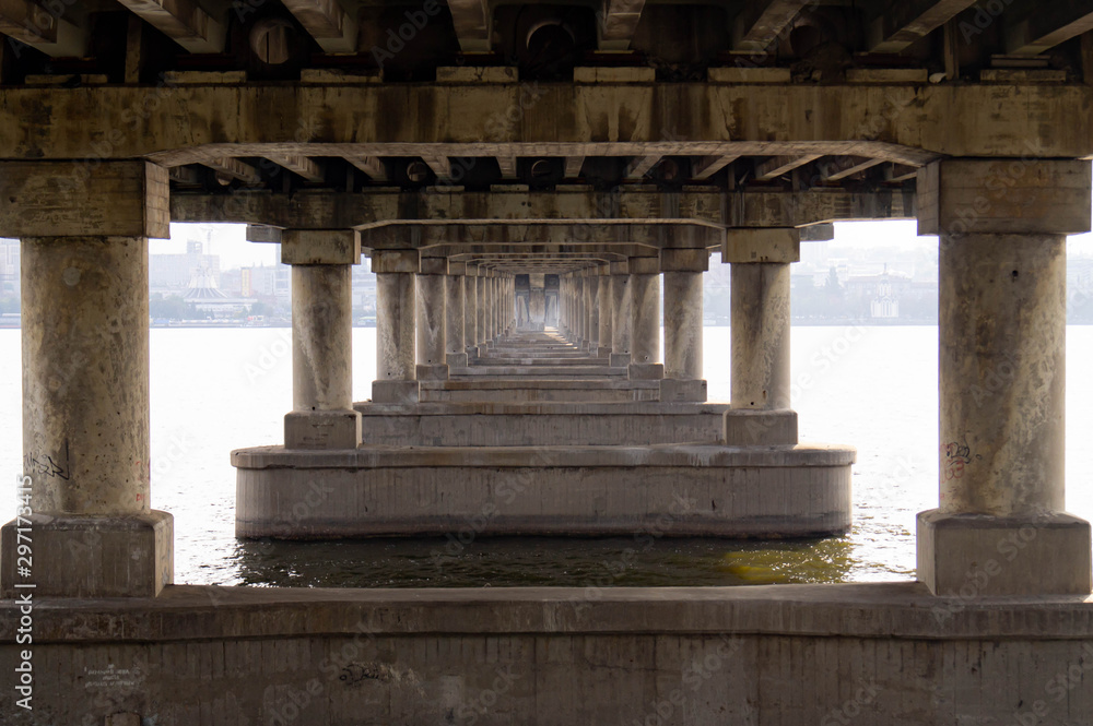 Fototapeta premium Gallery of the columns of the bridge. Under the bridge over the river.