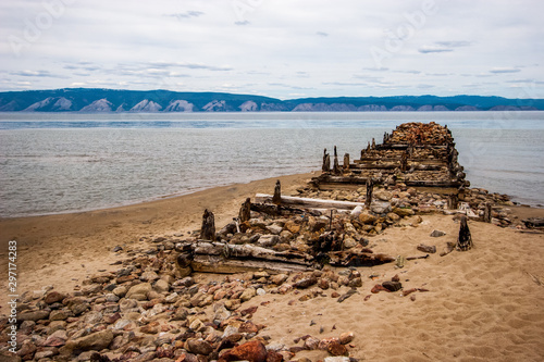 The destroyed old pier on the island of Olkhon on Lake Baikal. On the shore of stones and sand. Behind the mountain lake.