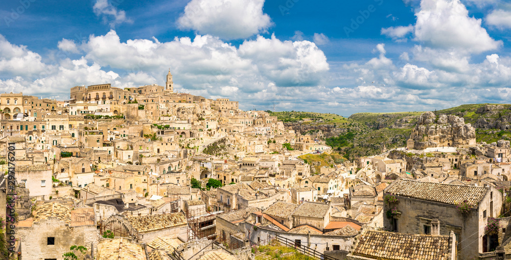 Aerial panoramic view of historical centre Sasso Caveoso of old ancient town Sassi di Matera with rock cave houses, blue sky white clouds, UNESCO World Heritage Site, Basilicata, Southern Italy