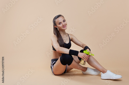 Young athletic girl brunette with black knee-pads sits on the floor, rests after a workout, takes a break.