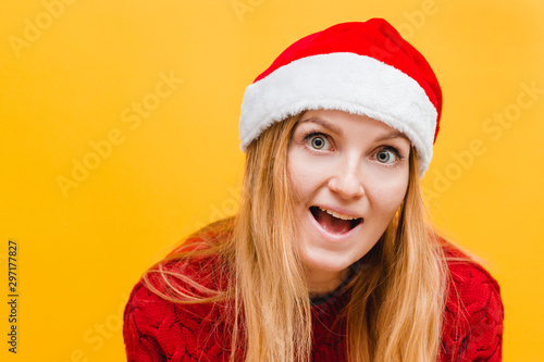 Happy excited young woman in santa claus hat over yellow background  place for text. Holiday concept.